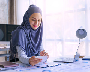 Young muslim woman working in business office, wearing Hijab works as start up SMEs project. Using...