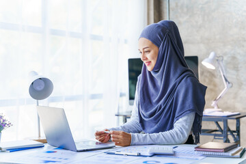 Young muslim woman working in business office, wearing Hijab works as start up SMEs project. Using...