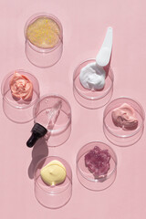 Fototapeta na wymiar Multicolored texture of cream, scrub and gel with a pipette in a Petri dish on a pink background. The concept of laboratory research of cosmetics. Smears of cosmetic skin care products.