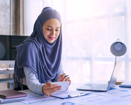 Young muslim woman working in business office, wearing Hijab works as start up SMEs project. Using calculator.