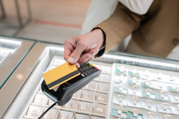 Cropped view of man paying with credit card near blurred girlfriend in jewelry shop.