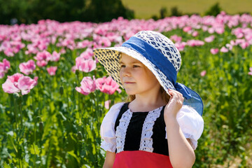 Little preschool girl in poppy field. Cute happy child in red riding hood dress play outdoor on blossom flowering meadow with pink poppies. Leisure activity in nature with children.