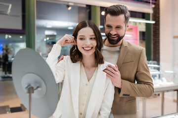 Smiling man hugging girlfriend with earring in jewelry shop.