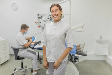 Obraz premium A woman dentist smiles at the camera on the background of a dental cabinet. Dental care and treatment concept