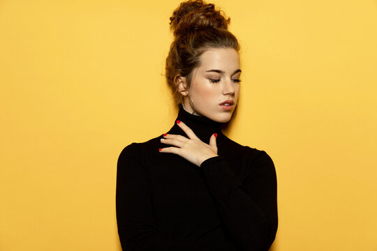 Portrait of georgeous girl posing for fashion photoshoot on yellow background. Pretty model dressed in stylish black pullover. Trend and lifestyle concept