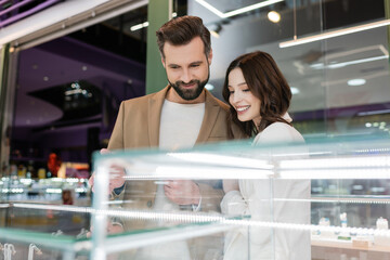 Fototapeta na wymiar Smiling couple looking at blurred showcase in jewelry shop.