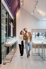 Smiling woman pointing with finger while walking with boyfriend in jewelry store.