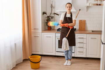 Fototapeta na wymiar Full length portrait of tired housewife washing floor at kitchen, pretty young woman doing home cleanup, keeping her apartment tidy, feeling overworked, looking at camera.
