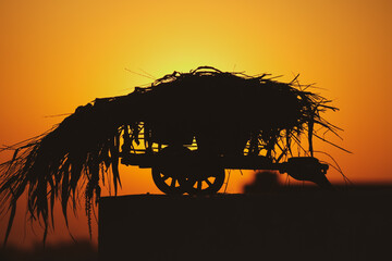 silhouette of a a bullock cart with cattle feed on it Indian village life