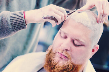 Obraz na płótnie Canvas Barber's hands working on the bald head of a bearded man.