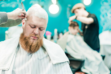 Barber is grooming a bald head of a bearded man.