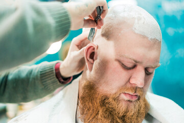Fototapeta premium A sleeping bearded client during shaving in barbershop.