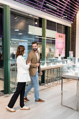 Smiling couple talking while walking near showcase in jewelry shop.