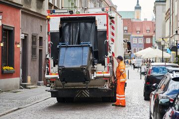 garbage and waste removal services. Worker loading waste bin into truck at city