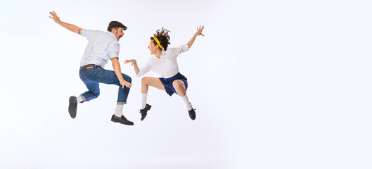 Portrait of young active couple, man and woman, dancing, jumping isolated over white studio background. Flyer