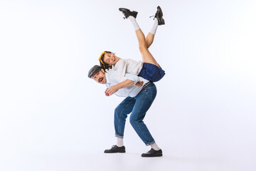 Portrait of young beautiful couple, man and woman, dancing, lifting girl on back isolated over white studio background