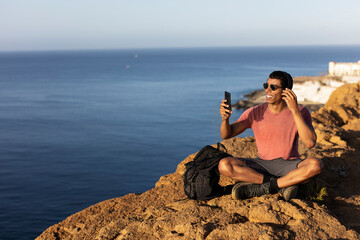 Young man sitting on the stone listening the music. Tourist man on the top of the mountain