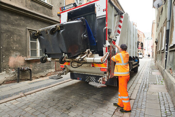 garbage and waste removal services. Worker loading waste bin into truck at city - 517642673