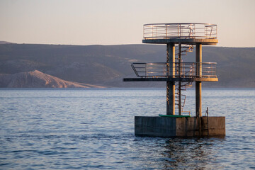 Diving tower in front of the sea with mountains in the background.