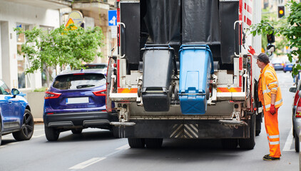garbage and waste removal services. Worker loading waste bin into truck at city - 517643283