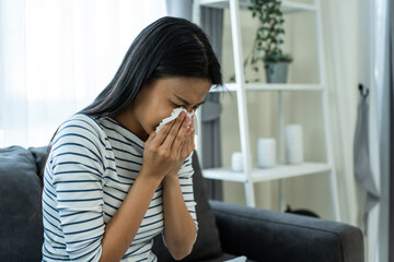 Asian beautiful woman having running nose and sneezing in living room.