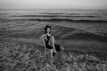 Artistic romantic portrait of a girl sitting on white chair at the sea. Black and white creative...
