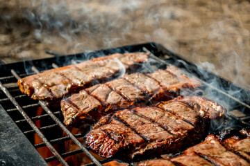 Beef steaks grilling on a cast iron grlill plate on a camp fire. Campfire cooking. Outdoor BBQ