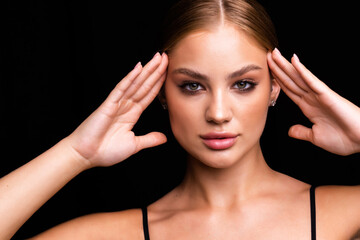 Fototapeta premium Portrait of young beautiful woman with evening make up touching her face over black background.