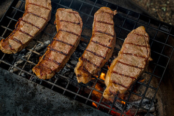 Beef steaks grilling on a cast iron grlill plate on a camp fire. Campfire cooking. Outdoor BBQ