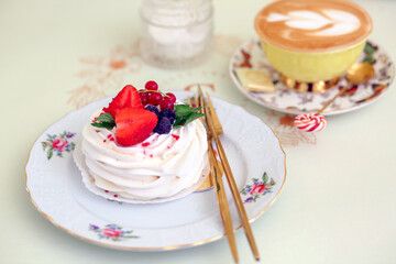 Sweet meringue dessert decorated with strawberries, blackberries and red currants and a cup of cappuccino. Confectionery. The concept of baking and desserts.