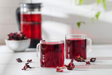 Herbal tea made from hibiscus petals in a transparent cup on a light background and a bowl of dry...