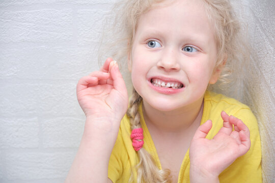 cute girl holding missing tooth, white wall background