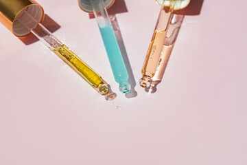 Three Pipettes with essential oil or beauty serum for face and body skin care on pink background...