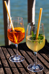 Hugo and Aperol Sprizz together on a wooden table, with the Ammersee in the background