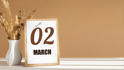 march 2. 2th day of month, calendar date.White vase with dead wood next to cork board with numbers. White-beige background with striped shadow. Concept of day of year, time planner, spring month