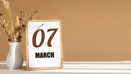 march 7. 7th day of month, calendar date.White vase with dead wood next to cork board with numbers. White-beige background with striped shadow. Concept of day of year, time planner, spring month