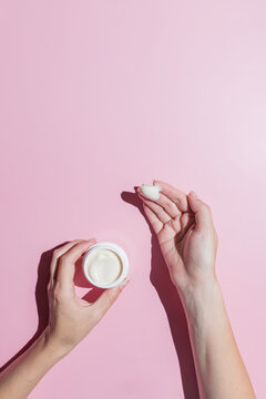 Woman applying the cream to the skin. Female hands with a white cream jar on a pink background close-up. Skin care cosmetics