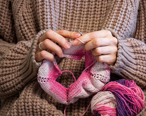 Knitting. Close-up girl's hands are knitting on knitting needles from pink yarn.