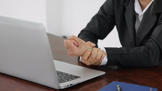 woman in office Holding her aching wrist caused by working on a computer laptop for a long time Carpal tunnel syndrome, arthritis, neurological disease concepts. hand numbness