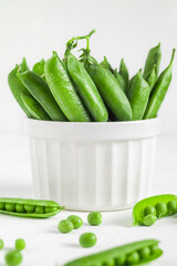Fresh green pods and green peas in a white bowl. Green pods and peas on a white background. Healthy eating concept. Organic raw produce.