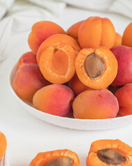 Whole and peeled orange apricots in a white plate on a kitchen table. Raw organic food.