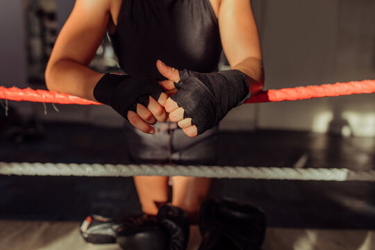 Female boxer standing with her hands wrapped in black in a boxing ring