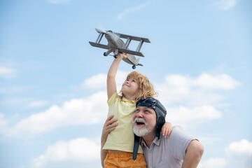Grandfather and grandson enjoying play with plane together on blue sky. Cute child with granddad playing outdoor.