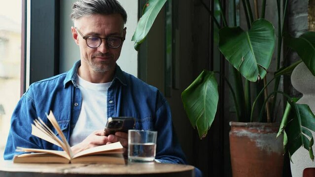 Laughing grey haired man typing on phone while sitting in cafe