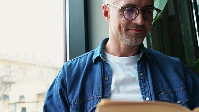 Grey haired concentrated man reading book indoors in cafe