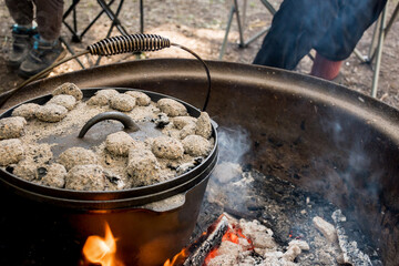Dutch oven camp cooking with coal briquettes beads on top. Campfire in a firepit. Camping cooking