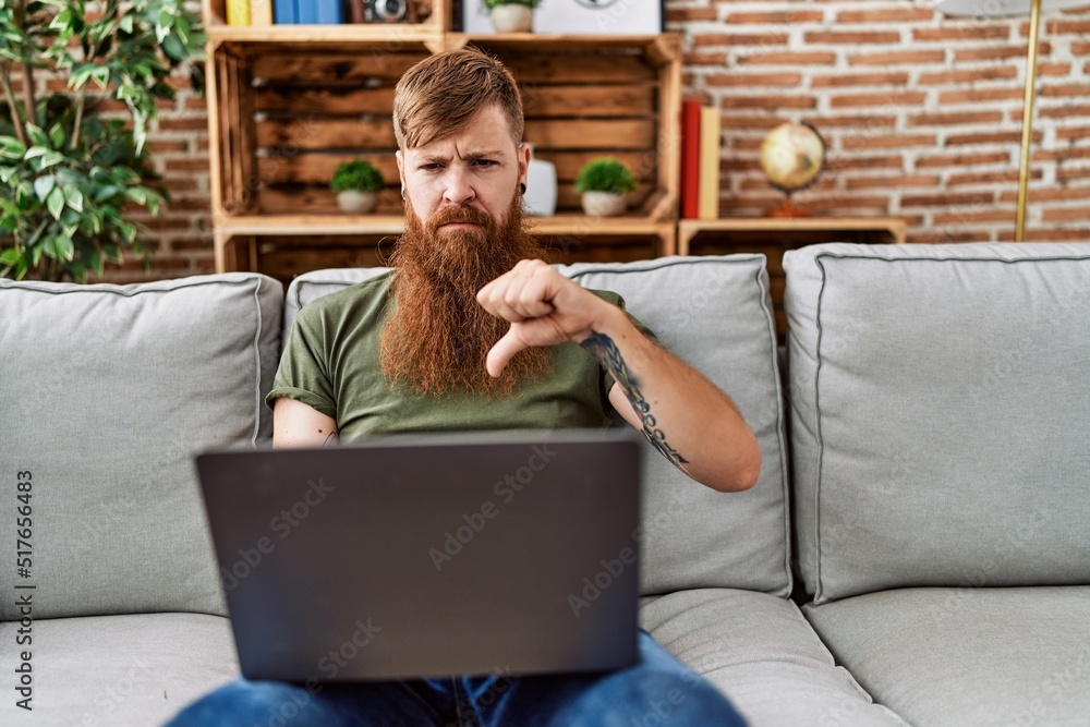 Canvas Prints redhead man with long beard using laptop sitting on the sofa at the living room with angry face, neg