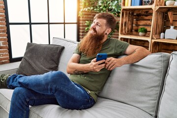 Obraz premium Young redhead man smiling confident using smartphone at home