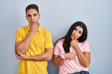 Young couple standing over isolated background looking confident at the camera smiling with crossed arms and hand raised on chin. thinking positive.