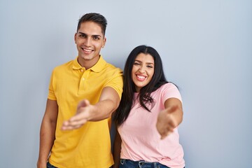 Fototapeta premium Young couple standing over isolated background smiling cheerful offering palm hand giving assistance and acceptance.